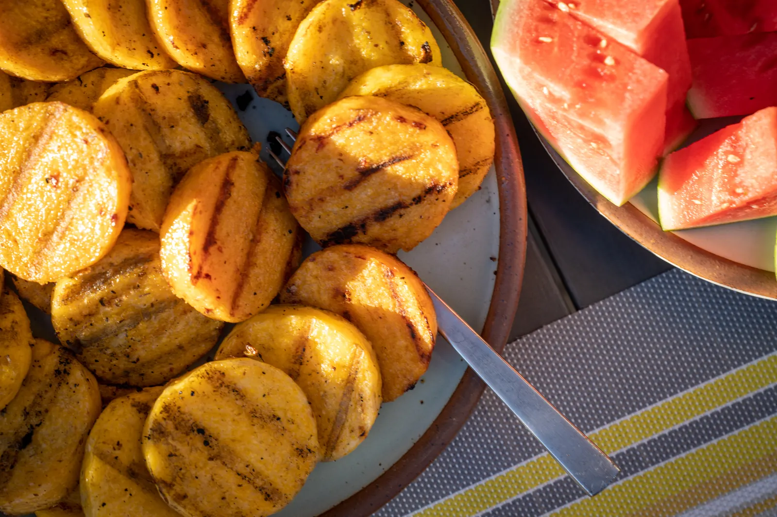 Grilled polenta rounds on a platter beside watermelon.