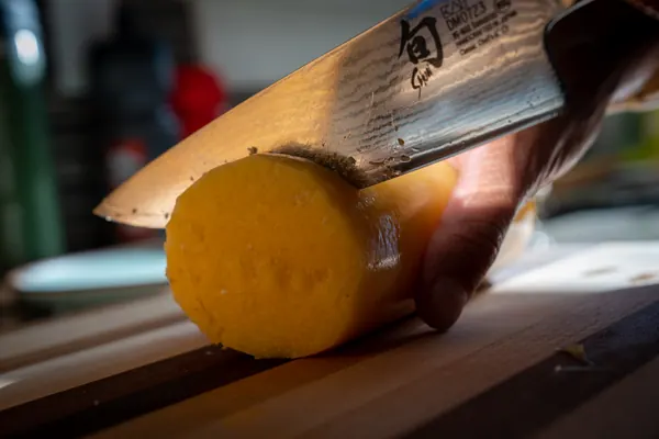 A knife slicing a polenta roll into rounds.