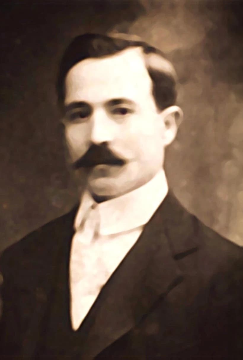 A studio portrait of Nicola DiIulio as a young man in a dark suit and tie.