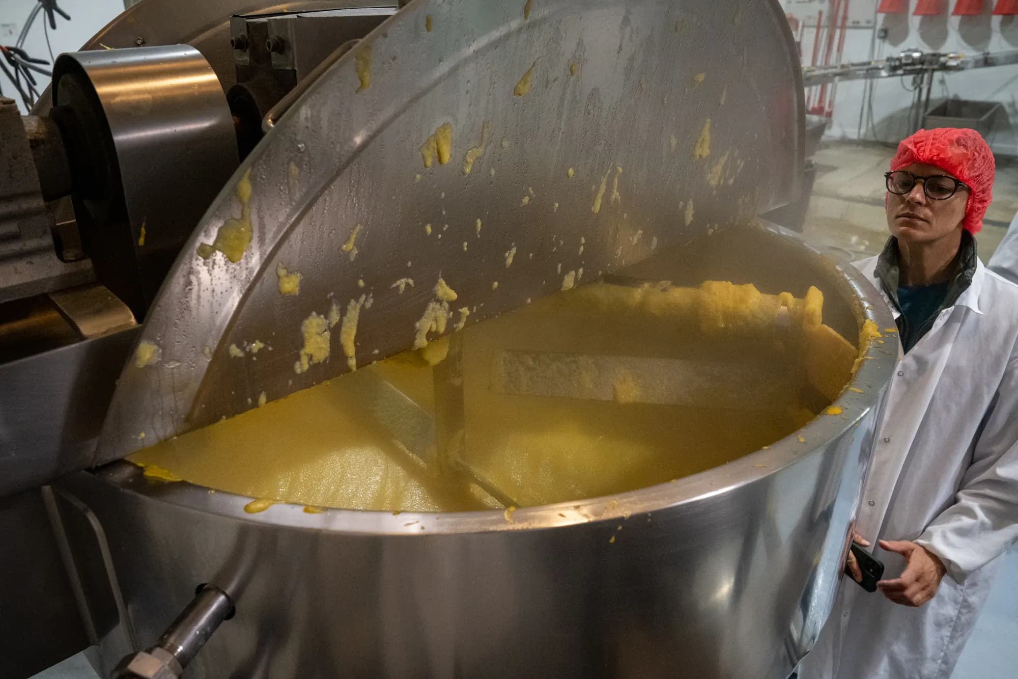 A paddle turns polenta in a steel kettle while a worker in a hairnet watches.