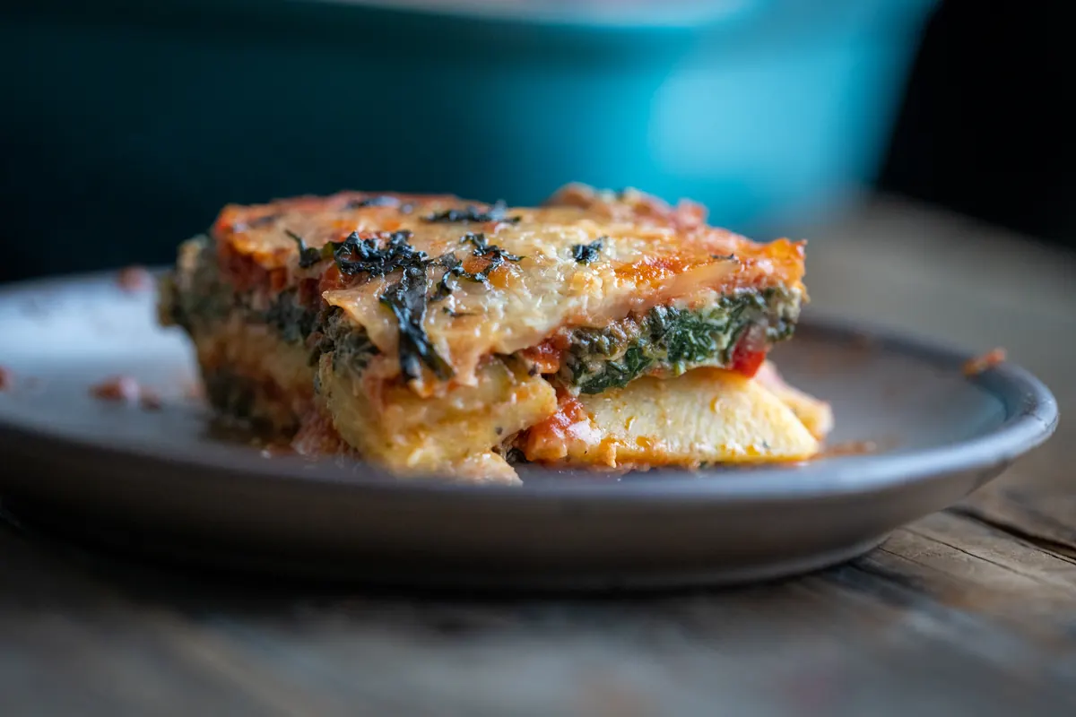 A slice of polenta lasagna on a gray plate showing layers of polenta, spinach and cheese.