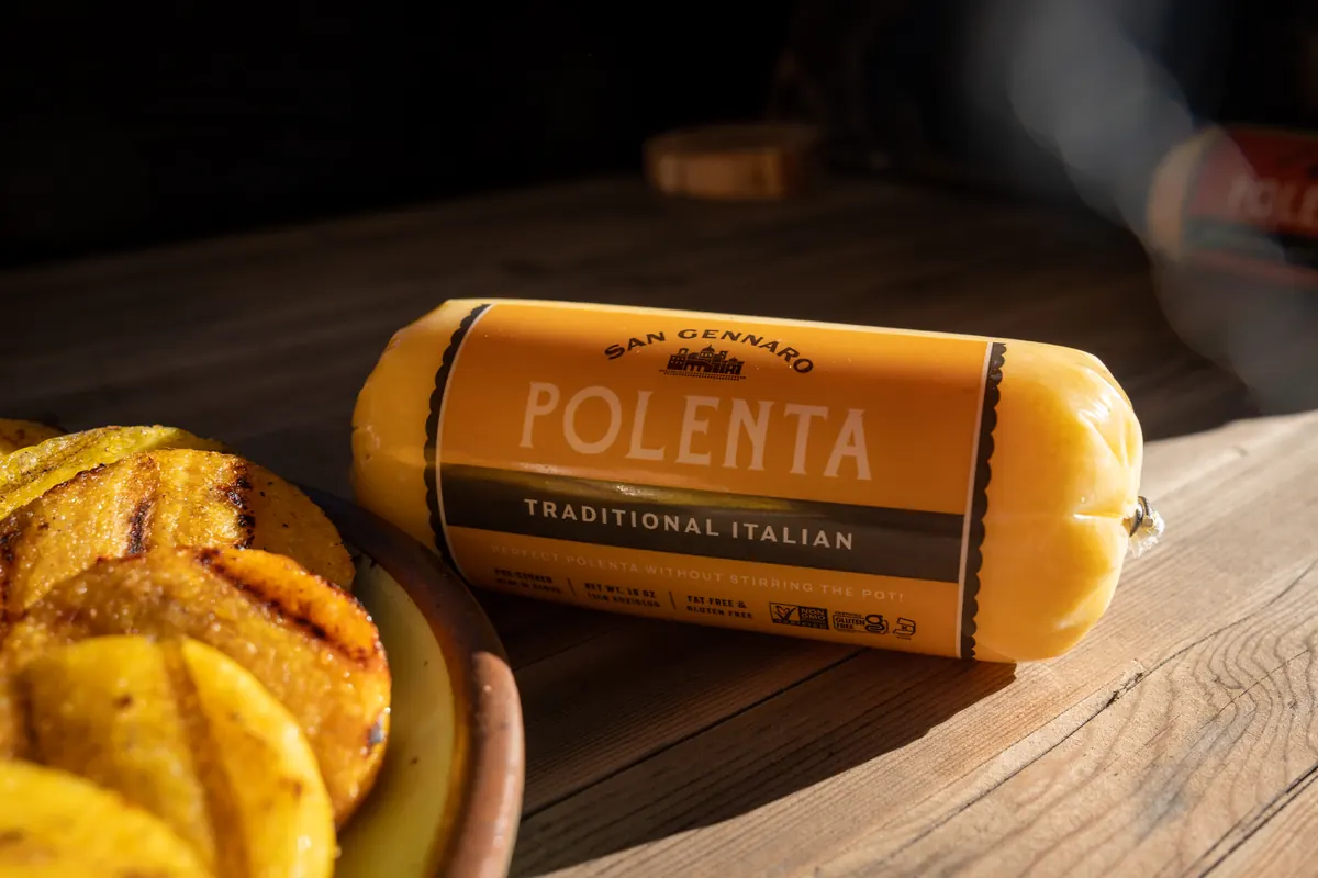 A roll of Traditional Italian polenta on a wood table beside grilled rounds.