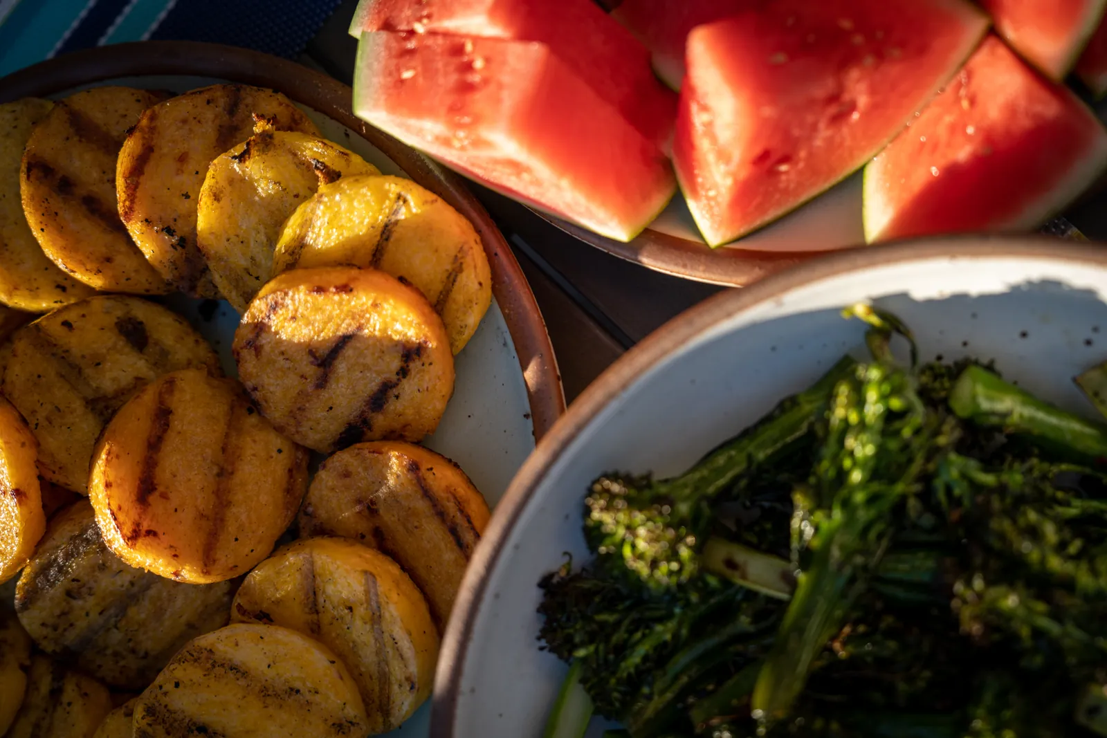 Grilled polenta rounds on a plate beside watermelon and charred broccolini.