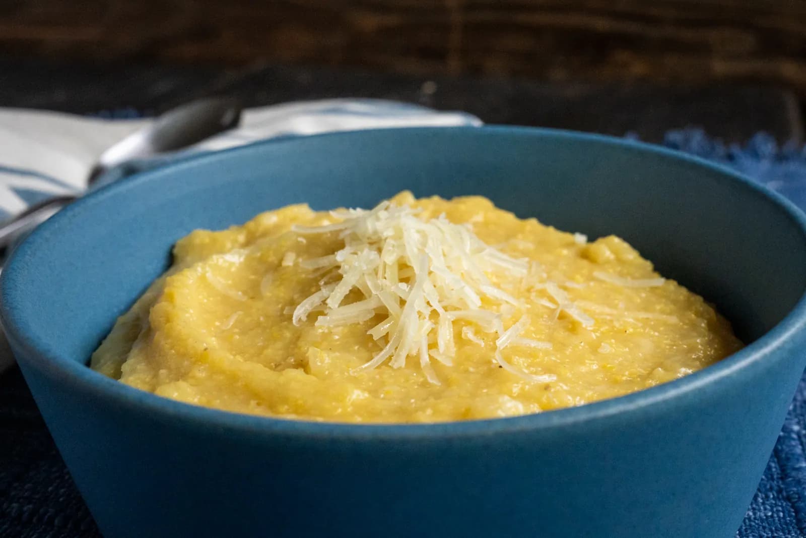 Creamy polenta topped with shredded parmesan in a blue bowl.